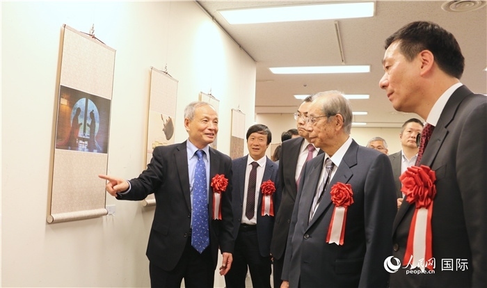 “湖州印象”攝影展主創(chuàng)、世界華人攝影協(xié)會副會長馮學(xué)敏向吳江浩大使、福田康夫前首相等嘉賓介紹展出作品。（人民網(wǎng) 許可攝）