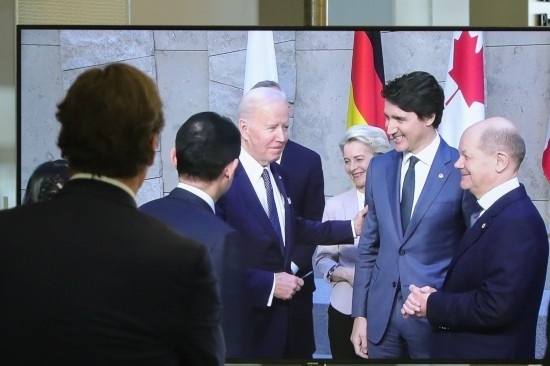 2022年3月24日，在比利時布魯塞爾的北約總部，一名男子觀看屏幕上美國總統(tǒng)拜登（右四）、歐盟委員會主席馮德萊恩（右三）、加拿大總理特魯多（右二）、德國總理朔爾茨（右一）出席七國集團(tuán)峰會合影儀式的畫面。新華社記者鄭煥松攝