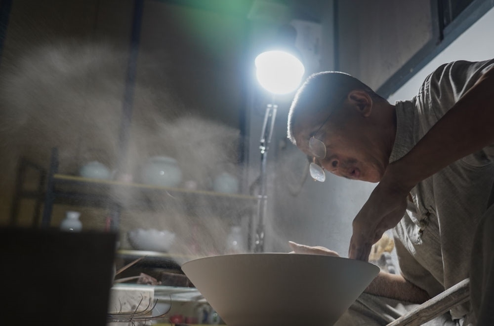 ↑ 在景德鎮(zhèn)，手工匠人吹去坯內(nèi)的泥土（2021年7月14日攝）。