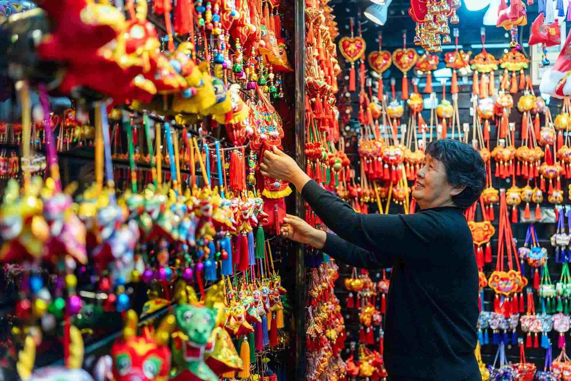 2023年12月11日，金華義烏國際商貿(mào)城，龍年喜慶用品掛滿攤位，顧客正在挑選中。