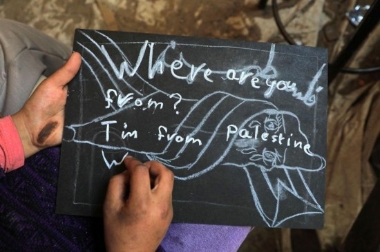 2023年12月28日，一名學生在加沙地帶南部城市拉法一所學校的臨時教室中寫下“我來自巴勒斯坦”的字樣。新華社發(fā)（里澤克·阿卜杜勒賈瓦德攝）