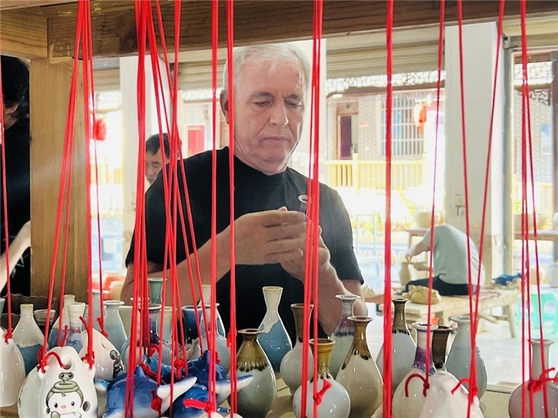 鄉(xiāng)愁如同一根根紅線，將游子與故鄉(xiāng)永遠地牽連到一起?；逄账囄幕瘎?chuàng)意一條街的母氏陶藝館內(nèi)，紅線吊著陶瓶，思緒游走萬里。摩爾多瓦“信息標簽”通訊社社長亞歷山大·塔納斯端詳著館內(nèi)展示的陶藝作品，并挑選出心儀的小擺件帶回摩爾多瓦，也帶走花茂村的“鄉(xiāng)愁”。（張亞欣攝）