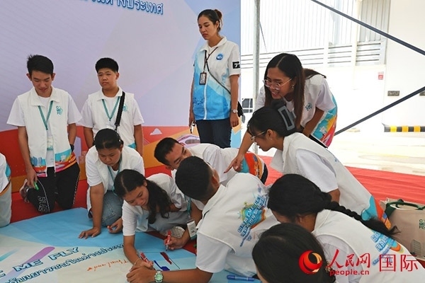 泰國學(xué)生在開營儀式展板上繪制圖案。人民網(wǎng)記者 白元琪攝