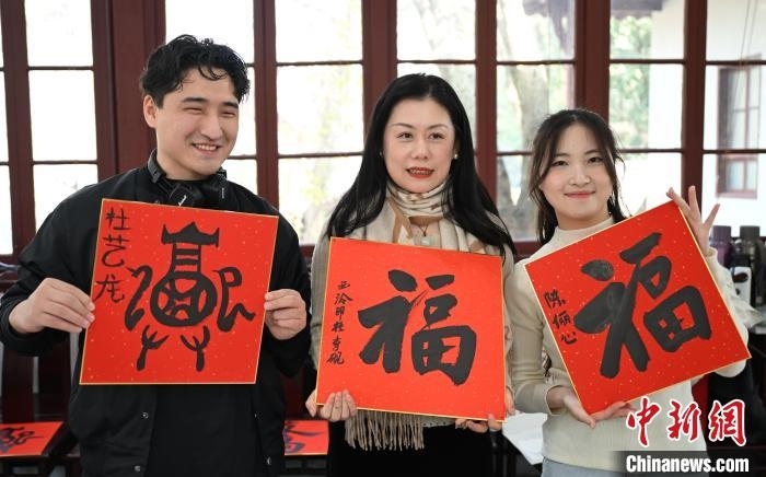 1月20日，外籍留學(xué)生和西泠印社社員李硯(中)展示各自創(chuàng)作的福貼。當日，來自巴西、馬來西亞、加納、哈薩克斯坦的外籍留學(xué)生在浙江杭州西泠印社體驗福貼、春聯(lián)和篆刻，感受古老的中國傳統(tǒng)文化。中新社記者 王剛 攝