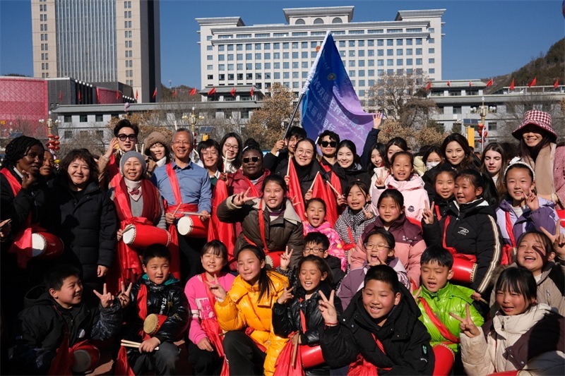 中外青年學(xué)子在安塞文化廣場觀看陜北腰鼓和大秧歌表演后合影留念，大家踏著鼓點共舞，翻飛的紅綢與躍動的身影交織，在黃土地廣場上繪出一幅生動的陜北民俗互動畫卷